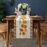 La table de salle à manger a un joli décor automnal avec un chemin de table imprimé de feuilles d'érable jaunes et orange, des fleurs blanches dans un vase et des verres à vin.