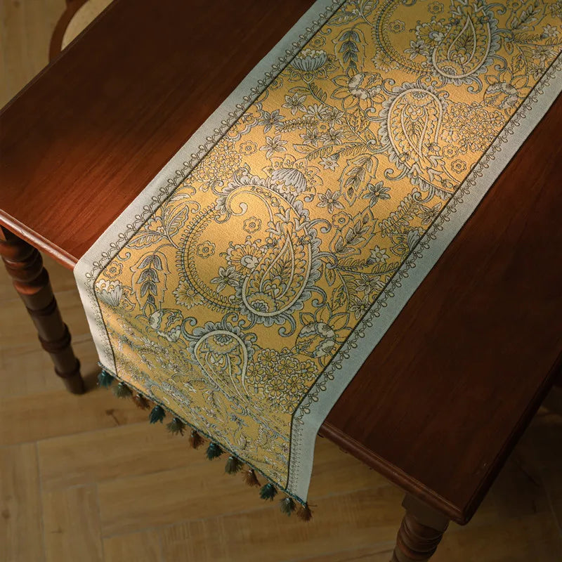 Un élégant chemin de table orné de motifs floraux et de motifs cachemire en jaune et bleu, sur un fond brun clair.