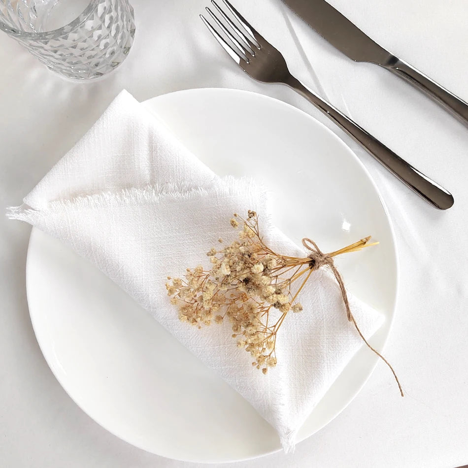 Arrangement élégant de fleurs séchées sur une assiette blanche, avec une serviette en lin et des couverts en métal, créant une atmosphère raffinée.
