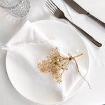 Arrangement élégant de fleurs séchées sur une assiette blanche, avec une serviette en lin et des couverts en métal, créant une atmosphère raffinée.