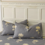 Ensemble de coussin décoratif avec motif de palmiers dorés sur fond gris, disposé sur un mur boisé orné de moulures sculptées.