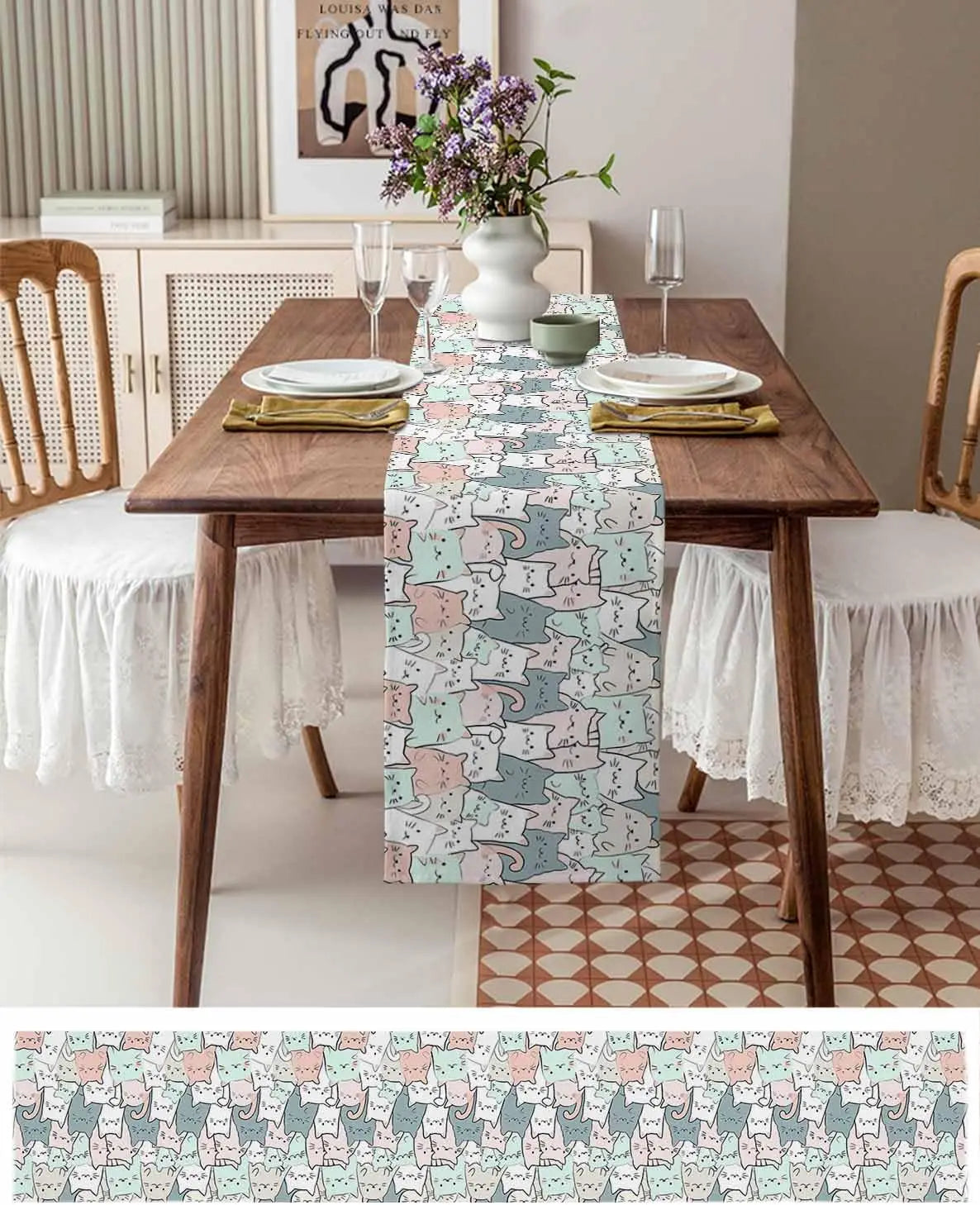 Une table à manger élégante avec une nappe à motifs de chats multicolores, des assiettes et des verres, et un vase rempli de fleurs violettes.