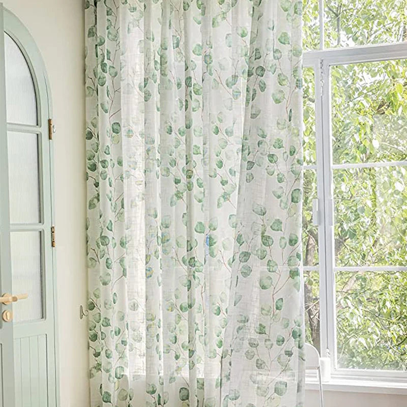 Zoom sur les voilages feuillage suspendus devant une fenêtre avec vue sur un arbre en extérieur.