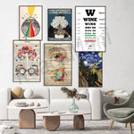 Dans cette image, on peut voir un mur décoré avec diverses affiches et œuvres d'art, notamment des éléments liés à l'optométrie et à l'art du tatouage, ainsi qu'une affiche humoristique sur le vin. Le salon est meublé de manière minimaliste avec des canapés blancs, une table basse en bois et un fauteuil gris, créant une atmosphère sereine et épurée.