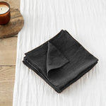 Serviettes de table noires pliées sur une surface en bois clair avec une bougie allumée à proximité, créant une atmosphère apaisante et élégante.