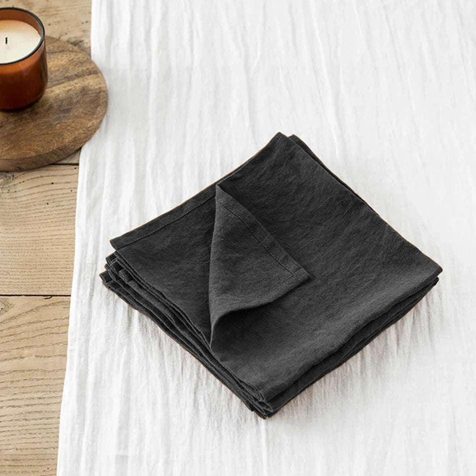 Tissu de lin noir plié sur une surface en bois avec une bougie allumée.