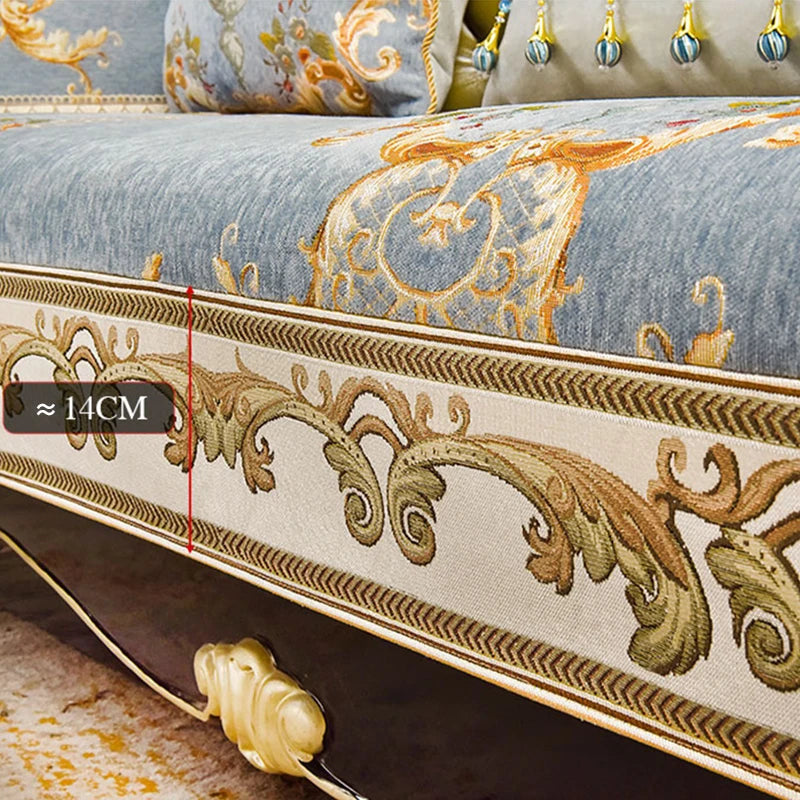Un couvre-lit décoratif avec des motifs ornementaux dorés sur un fond bleu grisâtre, avec des détails décoratifs tels que des glands dorés.