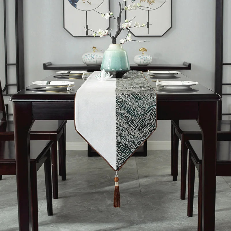 Cette image présente une belle table de salle à manger avec des assiettes, des accessoires décoratifs et un chemin de table patterné noir et blanc, créant une ambiance élégante et zen dans la pièce.