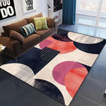 Le tapis coloré et géométrique au milieu du salon crée une ambiance moderne et élégante, complémentaire aux accents bruns et verts du canapé.