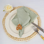 Arrangement élégant d'une assiette blanche avec une serviette vert clair, une rose blanche et un ornement décoratif en forme de goutte sur un napperon de paille tressée.