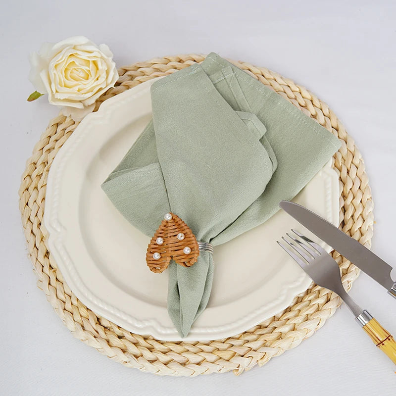 Arrangement élégant d'une assiette blanche avec une serviette vert clair, une rose blanche et un ornement décoratif en forme de goutte sur un napperon de paille tressée.