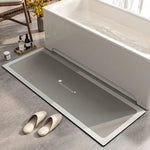 Tapis de bain gris élégant et épuré posé sur un sol carrelé près d'une baignoire blanche et d'accessoires de salle de bain.