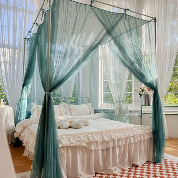 Lit à baldaquin invitant avec des rideaux translucides de couleur vert menthe dans une chambre lumineuse avec des fenêtres donnant sur un paysage verdoyant.