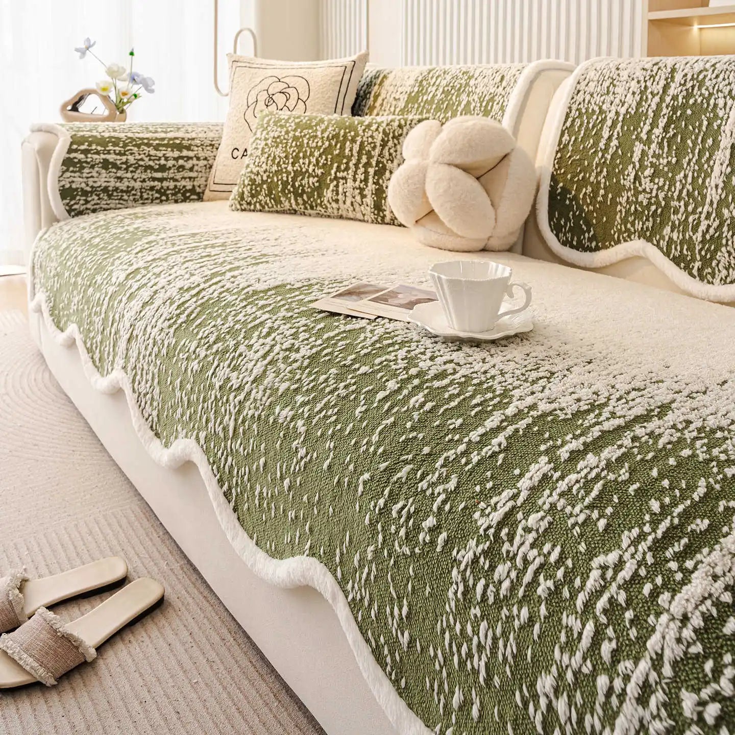 Un plaid douillet et confortable avec une texture texturée en vert et blanc, posé sur un canapé blanc, avec un coussin en forme de noeud et une tasse posée près, créant une ambiance cocooning et accueillante.