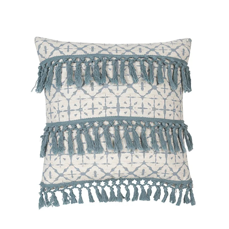 Coussin décoratif avec des motifs géométriques et des franges en textile bleu et blanc, créant une ambiance bohème et confortable.