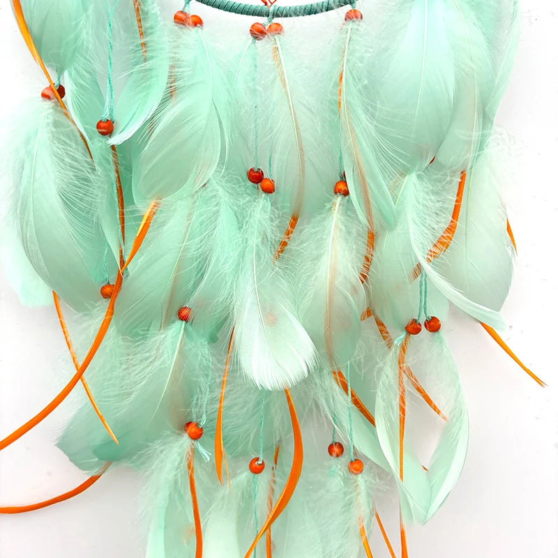 Délicat arrangement de plumes blanches et orange avec des perles rouges, créant une décoration suspendue élégante et délicate.