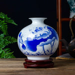Un vase en porcelaine blanche décoré de motifs floraux bleus élégants, posé sur un socle en bois.