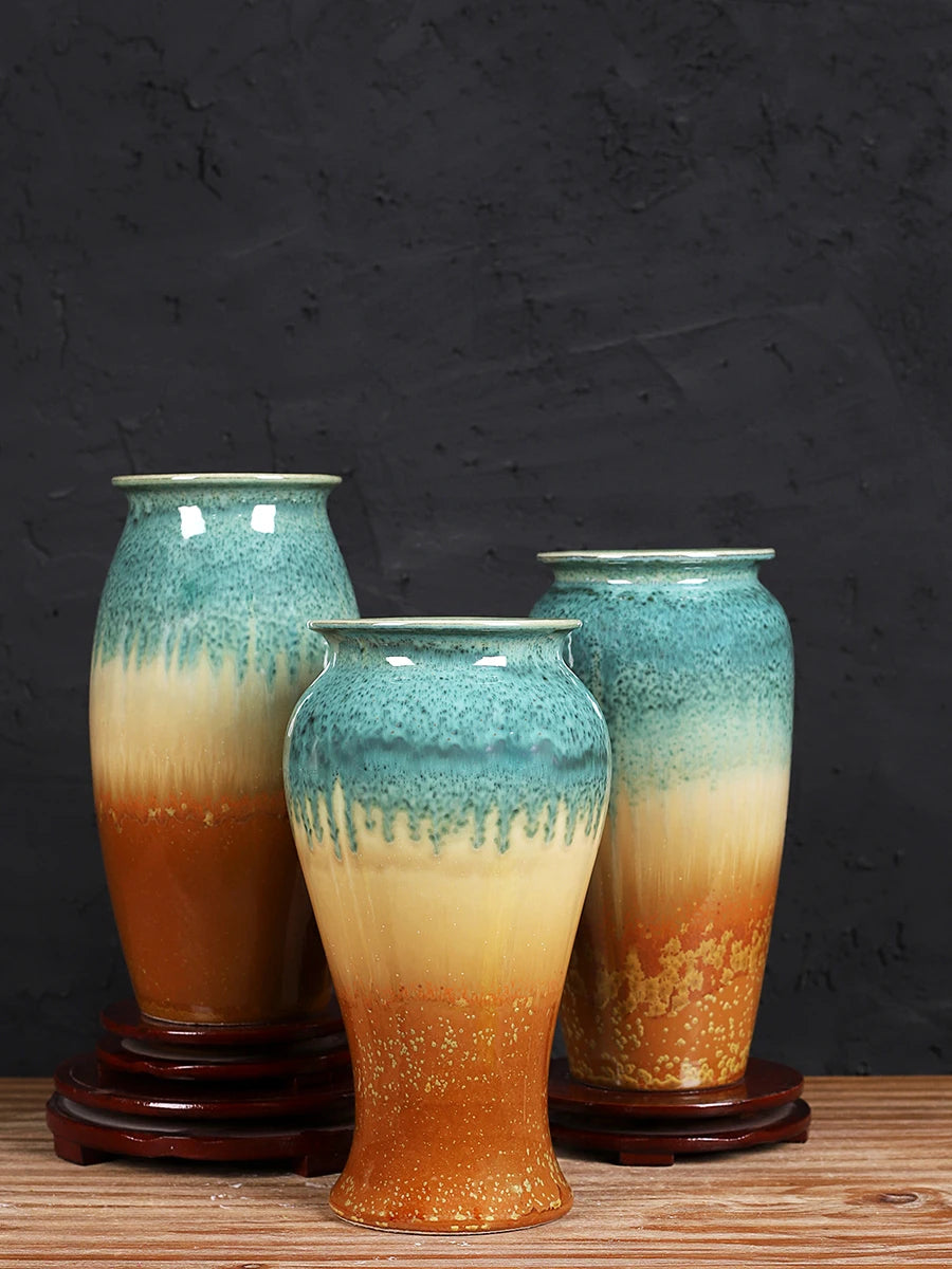 Des vases en céramique émaillée de couleurs vert-bleu et orange au fini lustré, sur un support en bois.