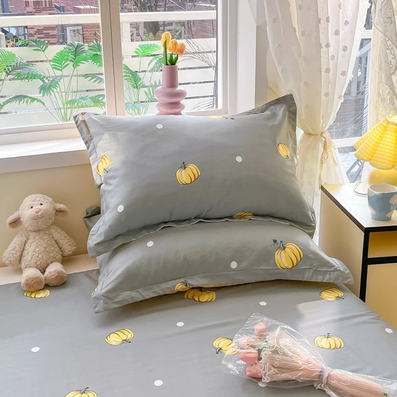 Ensemble de literie gris et jaune avec des motifs de citrouilles, posé sur une étagère avec des décorations et une peluche.