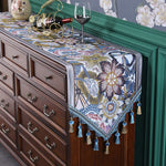 Meuble en bois brun foncé décoré d'un chemin de table aux motifs floraux colorés et de pompons décoratifs.