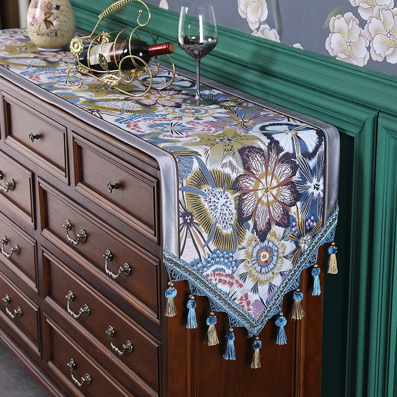 Meuble en bois brun foncé décoré d'un chemin de table aux motifs floraux colorés et de pompons décoratifs.