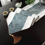 Tapis de table en tissu à motif vagues bleues et blanches, décoré d'une théière et de tasses de thé sur un plan de travail sombre.