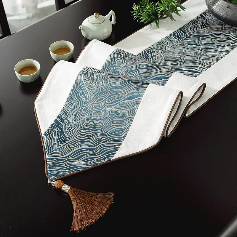 Tapis de table en tissu à motif vagues bleues et blanches, décoré d'une théière et de tasses de thé sur un plan de travail sombre.