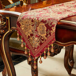 Une table de style baroque avec un magnifique chemin de table en motifs floraux dorés sur fond rouge, décoré de pompons et de perles.