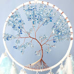 Un arbre de vie en cuivre aux branches étincelantes de cristaux bleu ciel, suspendu dans un cercle blanc, crée une œuvre d'art naturelle et éblouissante.