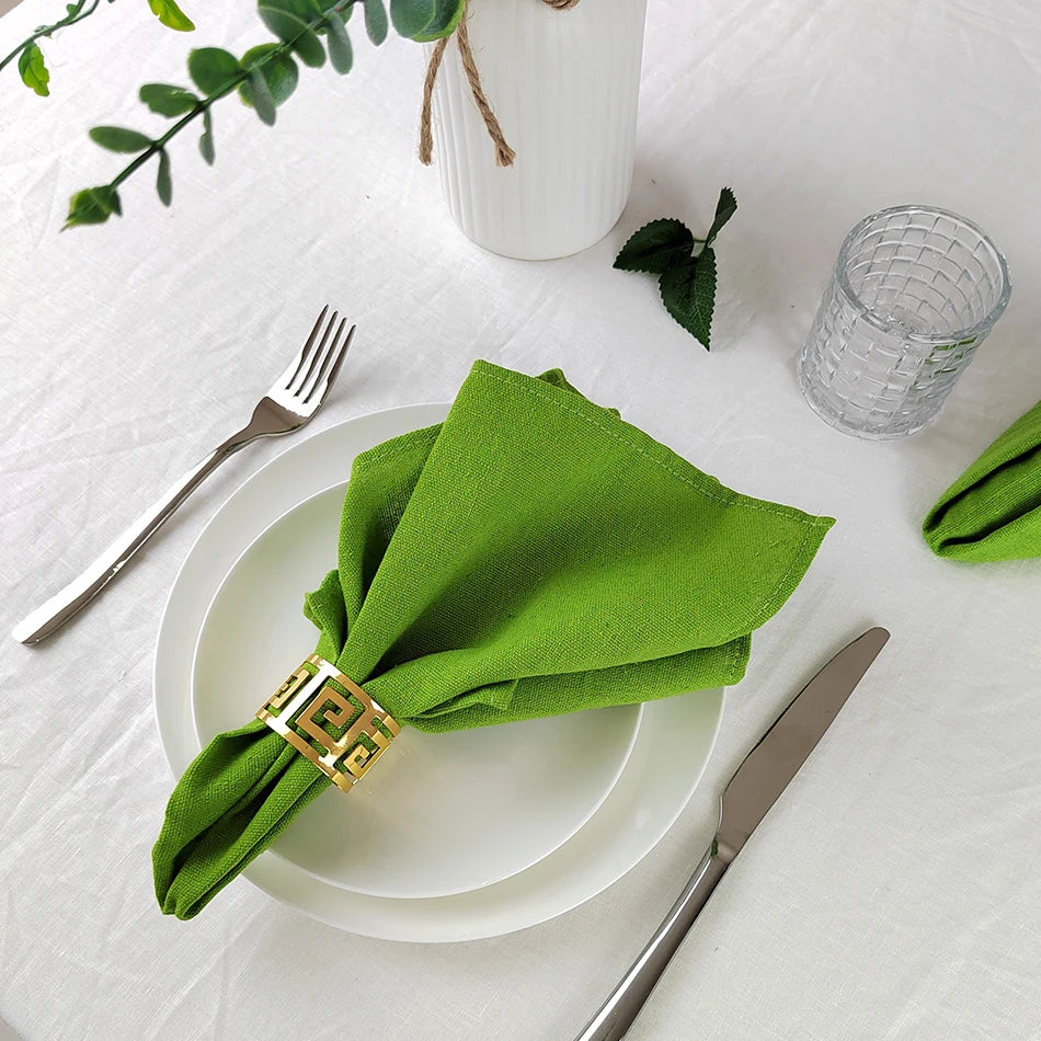 Cette image met en scène une décoration de table élégante avec une serviette en tissu vert, une assiette blanche, une fourchette et un couteau sur une nappe blanche, complétée par des éléments décoratifs tels qu'une bougie et un verre en cristal.