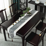 Une table à manger de style moderne avec des chaises noires, une nappe de table à motifs abstraits et un plateau central orné de plantes grasses.