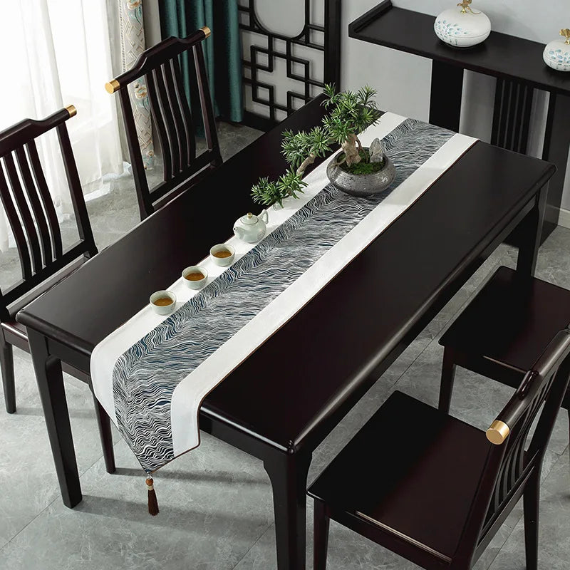 Une table à manger de style moderne avec des chaises noires, une nappe de table à motifs abstraits et un plateau central orné de plantes grasses.