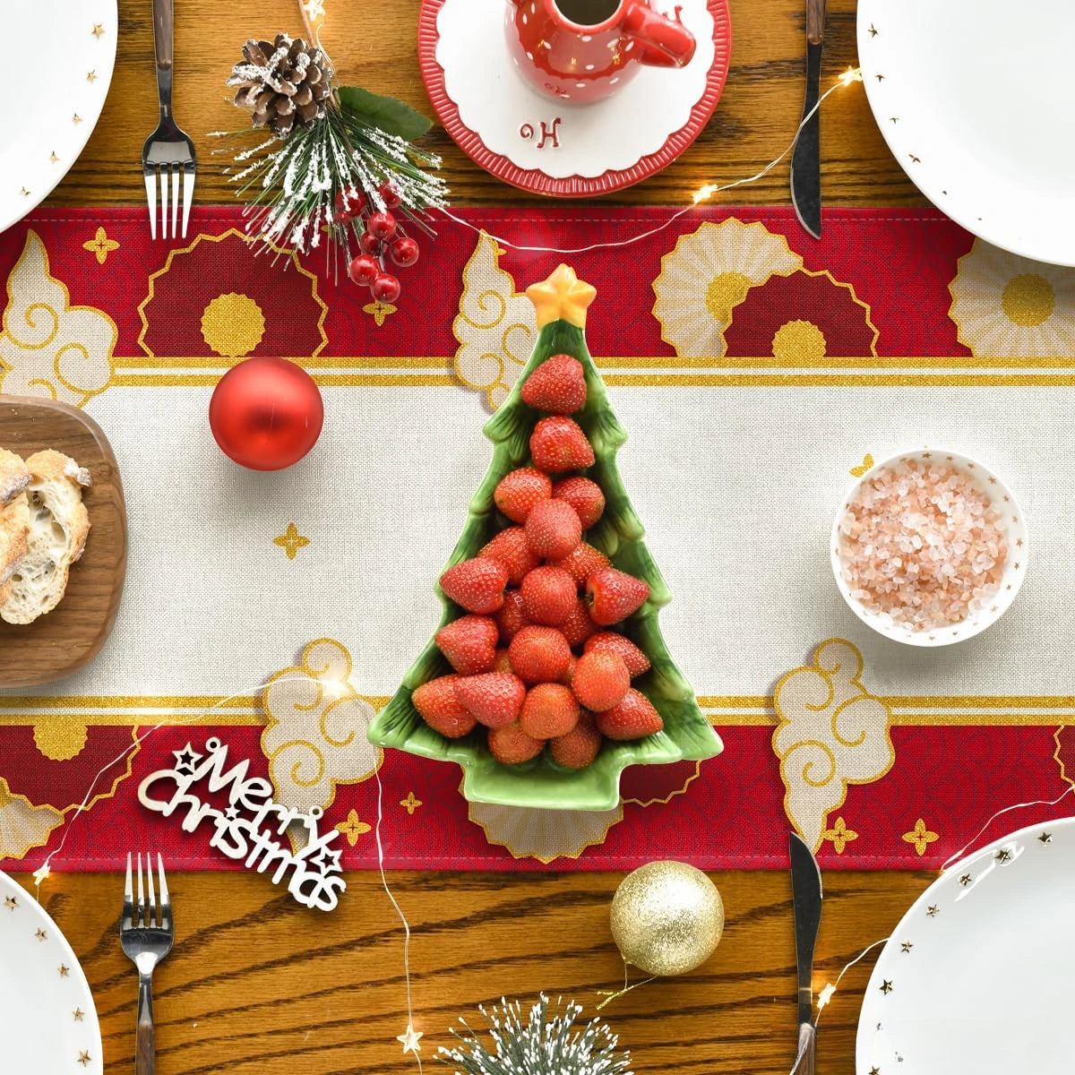 Une table de Noël élégamment décorée avec des fraises en forme d'arbre de Noël, des boules rouges, des accessoires dorés et un arrière-plan rouge et or.