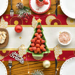 Une table de Noël élégamment décorée avec des fraises en forme d'arbre de Noël, des boules rouges, des accessoires dorés et un arrière-plan rouge et or.