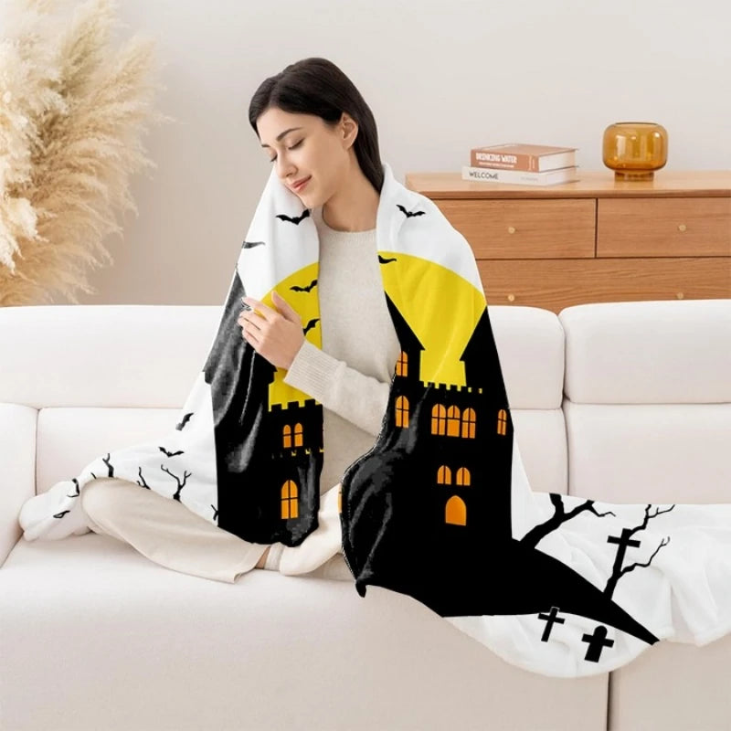 Une femme en tenue d'hiver enveloppée dans une couverture avec des motifs d'Halloween, assise sur un canapé confortable dans une pièce aux couleurs chaudes.