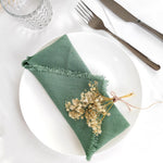 Une belle serviette verte avec des fleurs séchées disposées avec élégance sur un plat blanc, accompagnée de couverts en métal.