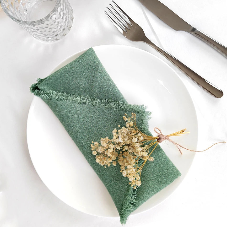 Une belle serviette verte avec des fleurs séchées disposées avec élégance sur un plat blanc, accompagnée de couverts en métal.