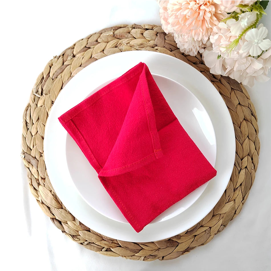 Serviette en feutre rouge posée sur une assiette blanche entourée d'un napperon tressé.