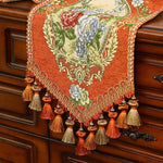 Un magnifique chemin de table orné de motifs floraux colorés et de pompons décoratifs, créant une atmosphère chaleureuse et élégante.