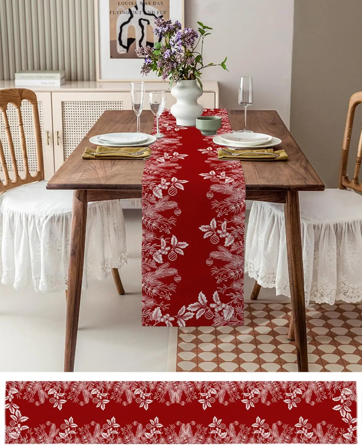 Cette image montre une table dressée avec des assiettes, des verres et un bouquet de fleurs violettes dans un vase blanc. Un chemin de table rouge motif floral blanc court le long de la table, qui est en bois sombre. Le sol est composé de carreaux blancs et marron.