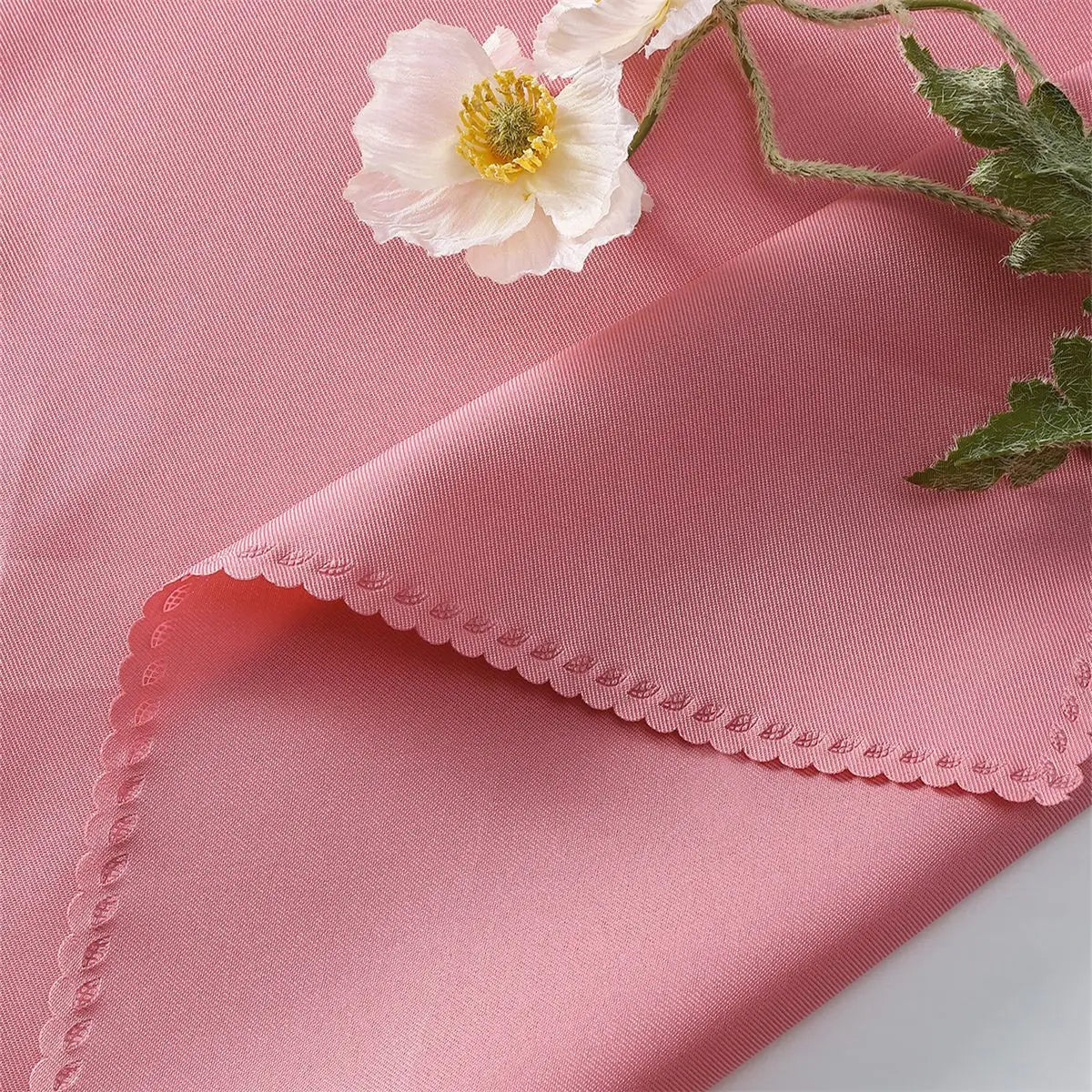 Une délicate fleur blanche aux pétales soyeux et à l'étamines dorées, reposant sur un fond rose pâle texturé.