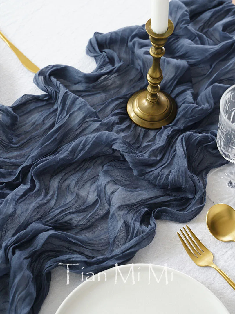 Cette image montre une table dressée avec de beaux tissus bleus soyeux, un chandelier doré et des couverts dorés sur une surface blanche, donnant une atmosphère élégante et sophistiquée.