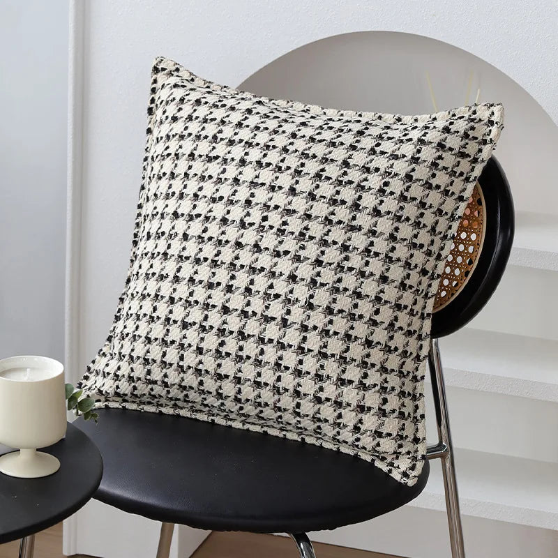 Coussin décoratif blanc et noir avec un motif géométrique sur un fauteuil dans un intérieur moderne.