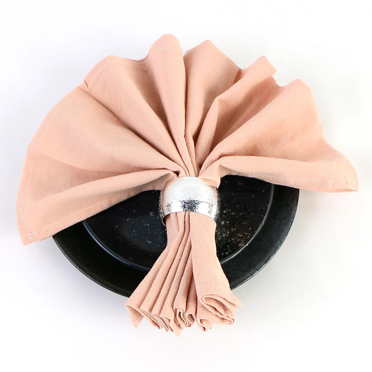 Serviette de table élégante pliée en forme de noeud papillon, avec un jonc argenté pour la maintenir, posée sur un plat noir.