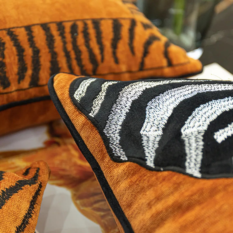 Un coussin décoratif aux motifs ethniques orange et noirs sur un canapé en bois crée une atmosphère chaleureuse et accueillante.