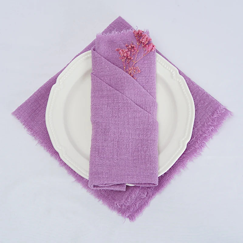Une serviette de table élégante et délicate de couleur lilas, disposée sur une assiette blanche pour un arrangement de table raffiné.