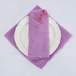 Une serviette de table élégante et délicate de couleur lilas, disposée sur une assiette blanche pour un arrangement de table raffiné.