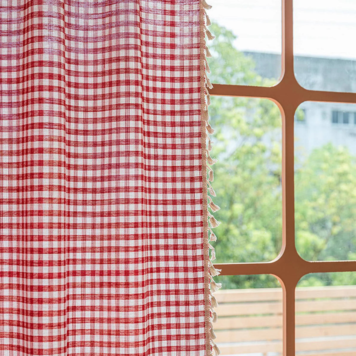 Rideau à carreaux rouges et blancs avec franges, suspendu près d'une fenêtre lumineuse. Parfait pour ajouter une touche de charme rustique à votre intérieur tout en offrant une touche de couleur vive à votre décoration.