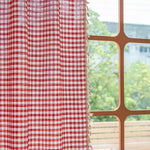 Rideau à carreaux rouges et blancs avec franges, suspendu près d'une fenêtre lumineuse. Parfait pour ajouter une touche de charme rustique à votre intérieur tout en offrant une touche de couleur vive à votre décoration.