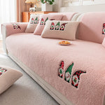 Cette image montre un canapé rose, avec des coussins décorés de motifs de lutins de Noël. Le canapé est placé dans un environnement confortable et cosy, avec des éléments de décoration qui apportent une touche festive à la pièce.